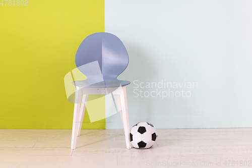 Image of modern blue chair and soccer ball in front of a blue green background