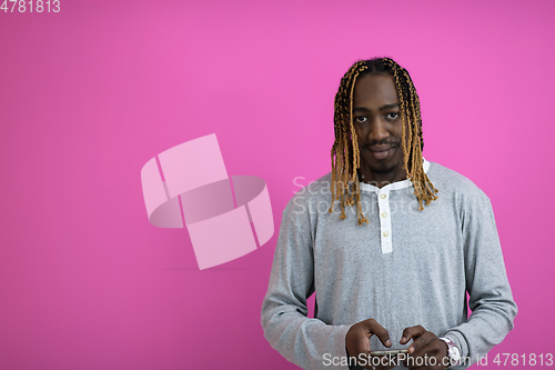 Image of afro guy uses a phone while posing in front of a pink background.