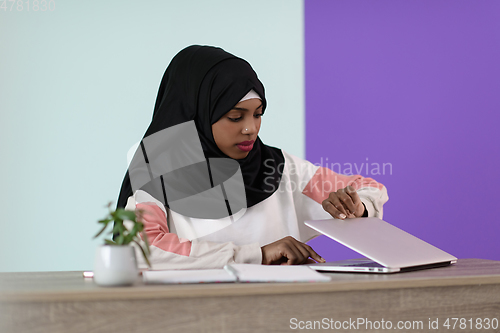 Image of afro girl wearing a hijab thoughtfully sits in her home office and uses a laptop