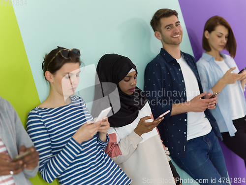 Image of diverse teenagers use mobile devices while posing for a studio photo in front of a pink background