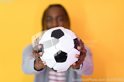 Image of afro man posing on a yellow background while holding a soccer ball