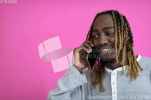 Image of afro guy uses a phone while posing in front of a pink background.