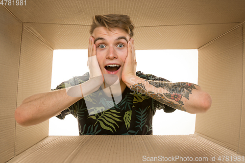 Image of Young man opening the biggest postal package isolated on white