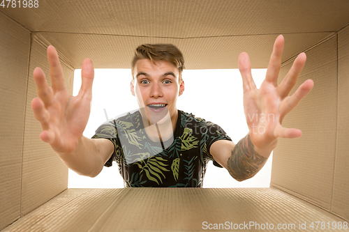 Image of Young man opening the biggest postal package isolated on white