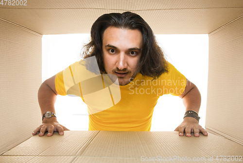 Image of Young man opening the biggest postal package isolated on white