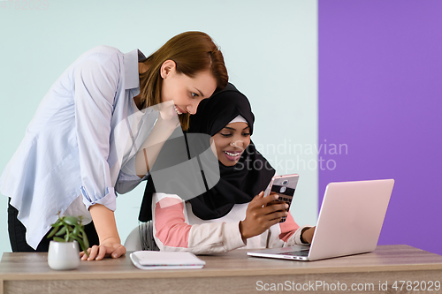 Image of afro girl with a hijab and a European woman use a cell phone and laptop in their home office