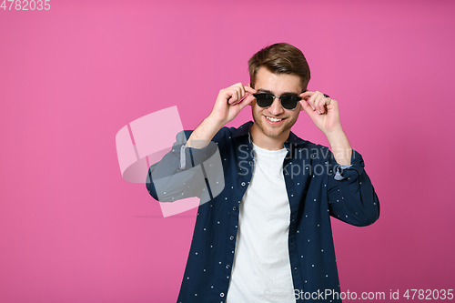 Image of a portrait of a young man wearing a blue shirt and posing in front of a pink background 