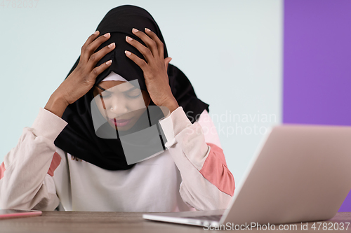 Image of afro girl wearing a hijab is disappointed and sad sitting in her home office and using a laptop