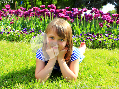 Image of school girl lays on the grass and besides tulips