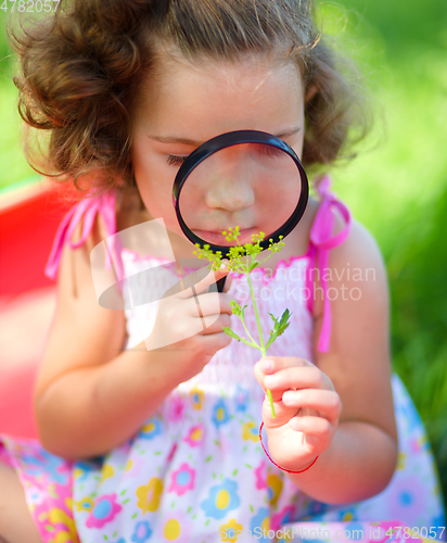 Image of Young girl is looking at flower through magnifier