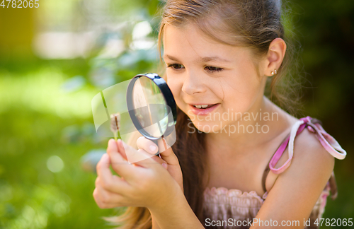 Image of Young girl is looking at flower through magnifier