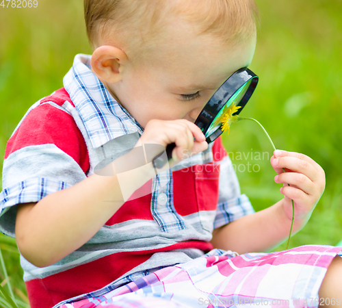 Image of Young boy is looking at flower through magnifier