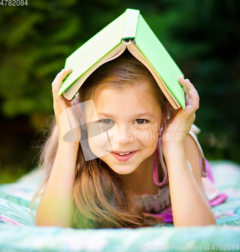Image of Little girl is hiding under book outdoors