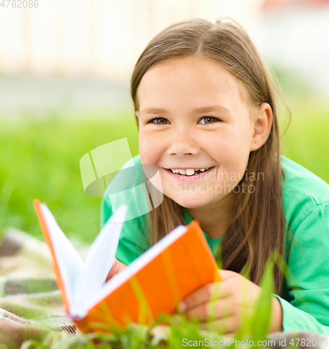 Image of Little girl is reading a book outdoors