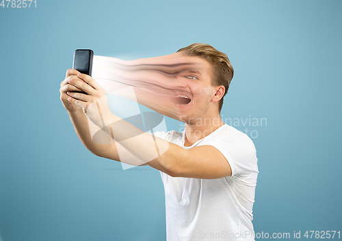 Image of Young man engaged by gadget and social media isolated on blue background
