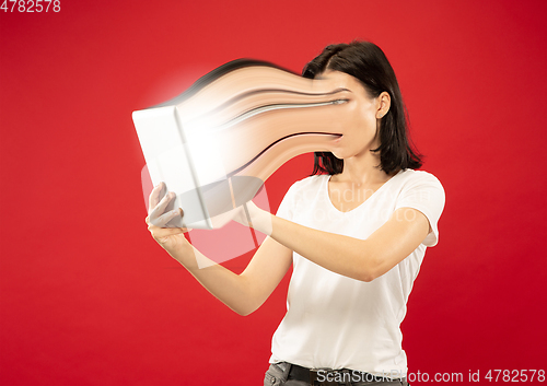 Image of Young woman engaged by gadget and social media isolated on red background