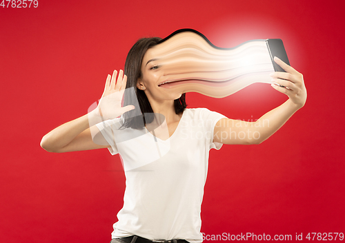 Image of Young woman engaged by gadget and social media isolated on red background