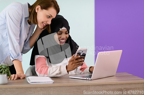 Image of afro girl with a hijab and a European woman use a cell phone and laptop in their home office