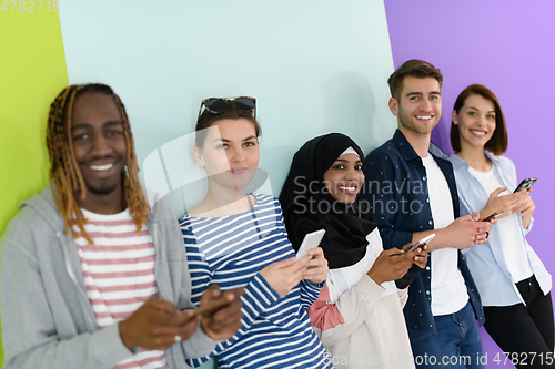 Image of diverse teenagers use mobile devices while posing for a studio photo in front of a pink background