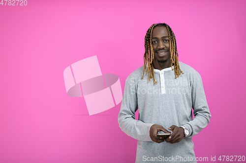 Image of afro guy uses a phone while posing in front of a pink background.