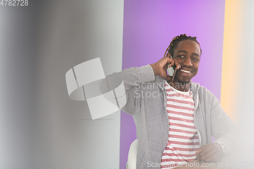 Image of afro young man sits in his home office during a pandemic and uses the phone