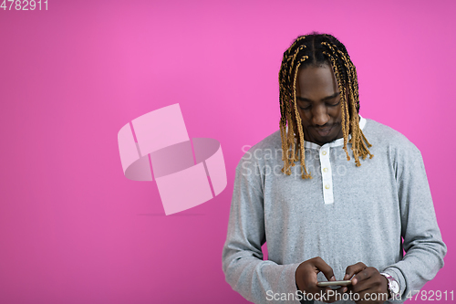 Image of afro guy uses a phone while posing in front of a pink background.