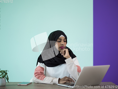 Image of afro girl wearing a hijab thoughtfully sits in her home office and uses a laptop