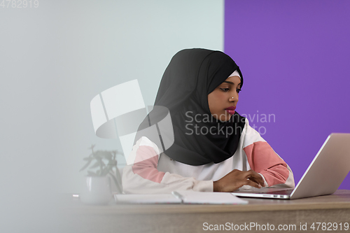 Image of afro girl wearing a hijab thoughtfully sits in her home office and uses a laptop