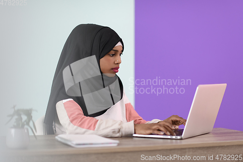 Image of afro girl wearing a hijab thoughtfully sits in her home office and uses a laptop