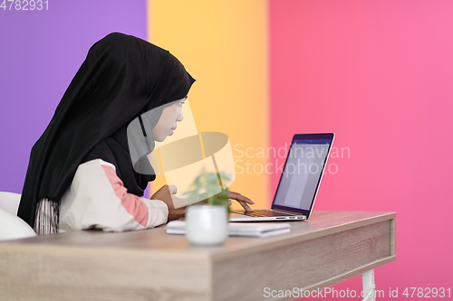 Image of afro girl wearing a hijab is disappointed and sad sitting in her home office and using a laptop