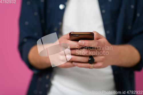 Image of a young man using a smartphone on a pink background.