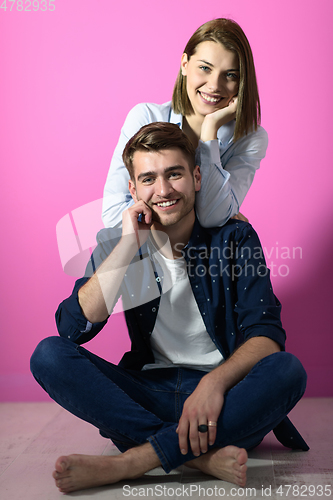 Image of couple sitting on the floor while posing in front of a pink background