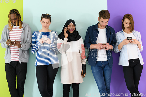 Image of diverse teenagers use mobile devices while posing for a studio photo in front of a pink background