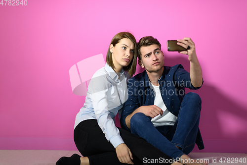 Image of a happy young couple sitting on the floor in the house and making selfie