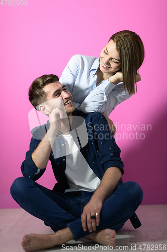 Image of couple sitting on the floor while posing in front of a pink background