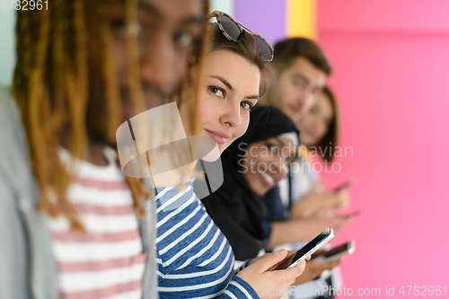 Image of diverse teenagers use mobile devices while posing for a studio photo in front of a pink background