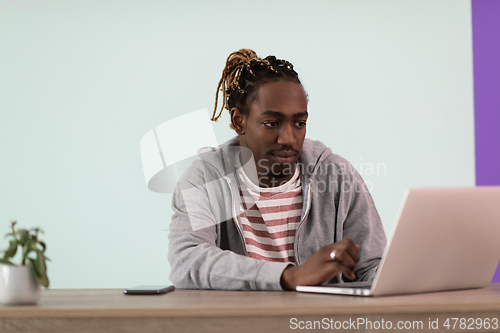 Image of an afro young man sits in his home office during a pandemic and uses laptop