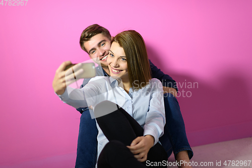 Image of a happy young couple sitting on the floor in the house and making selfie