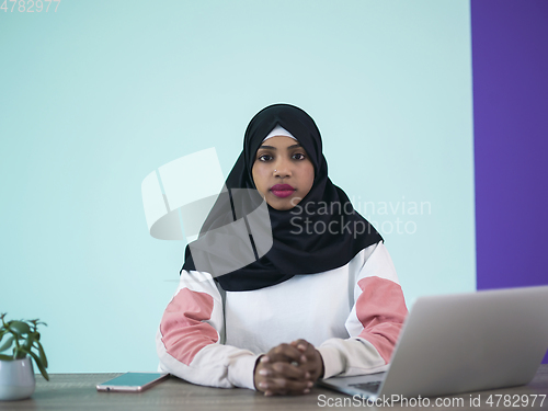 Image of afro girl wearing a hijab thoughtfully sits in her home office and uses a laptop