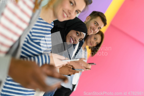 Image of diverse teenagers use mobile devices while posing for a studio photo in front of a pink background
