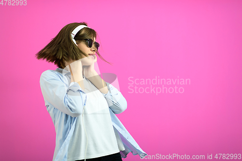 Image of brunette lady in black glasses dancing and listening music isolate on pink background