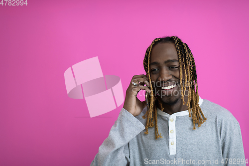 Image of afro guy uses a phone while posing in front of a pink background.