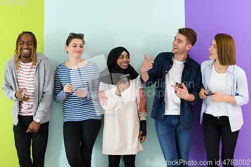 Image of diverse teenagers use mobile devices while posing for a studio photo in front of a pink background