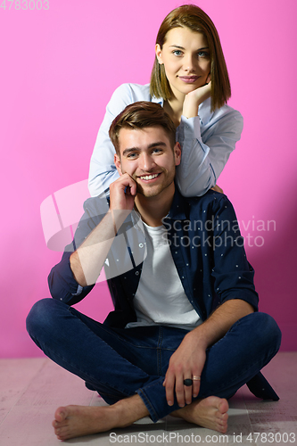 Image of couple sitting on the floor while posing in front of a pink background