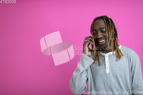 Image of afro guy uses a phone while posing in front of a pink background.