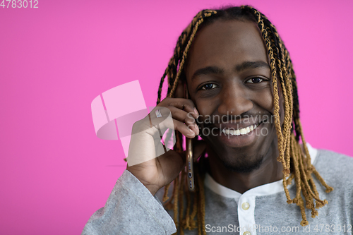 Image of afro guy uses a phone while posing in front of a pink background.