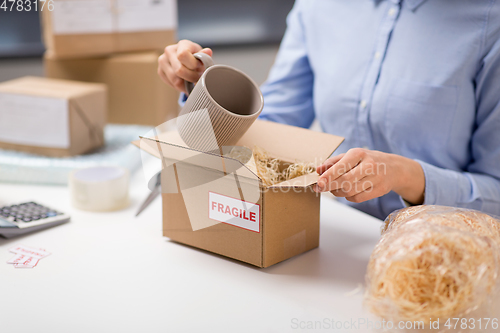 Image of woman packing mug to parcel box at post office