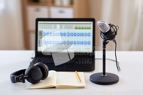 Image of microphone, laptop, headphones, notebook on table