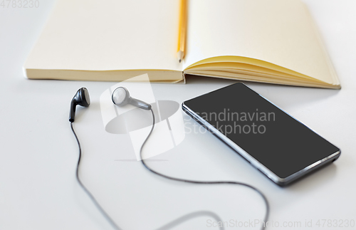 Image of earphones, smartphone and notebook with pencil