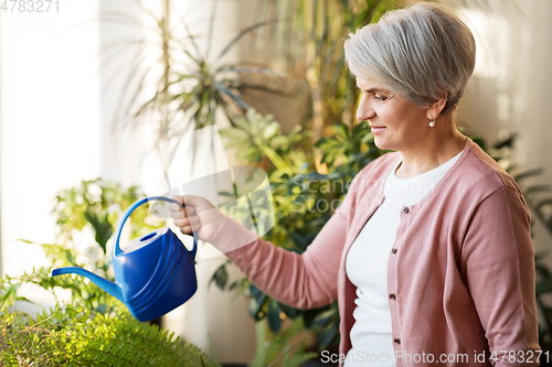 Image of senior woman watering houseplants at home